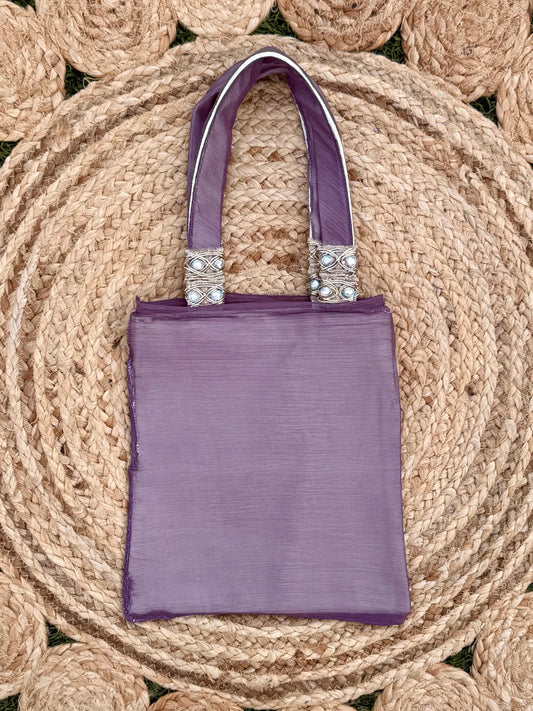 Purple handbag with decorative handles on a woven mat