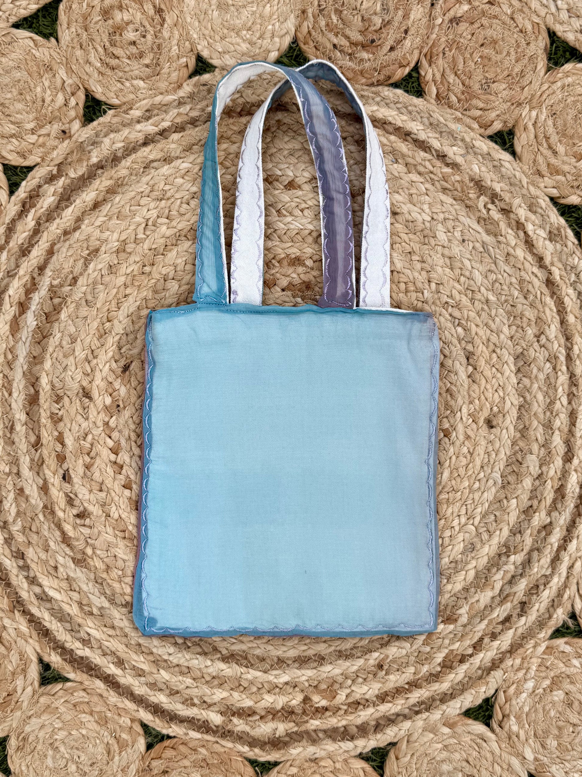Light blue tote bag with handles on a woven mat
