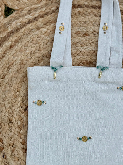 Light blue tote bag with decorative buttons on a woven surface