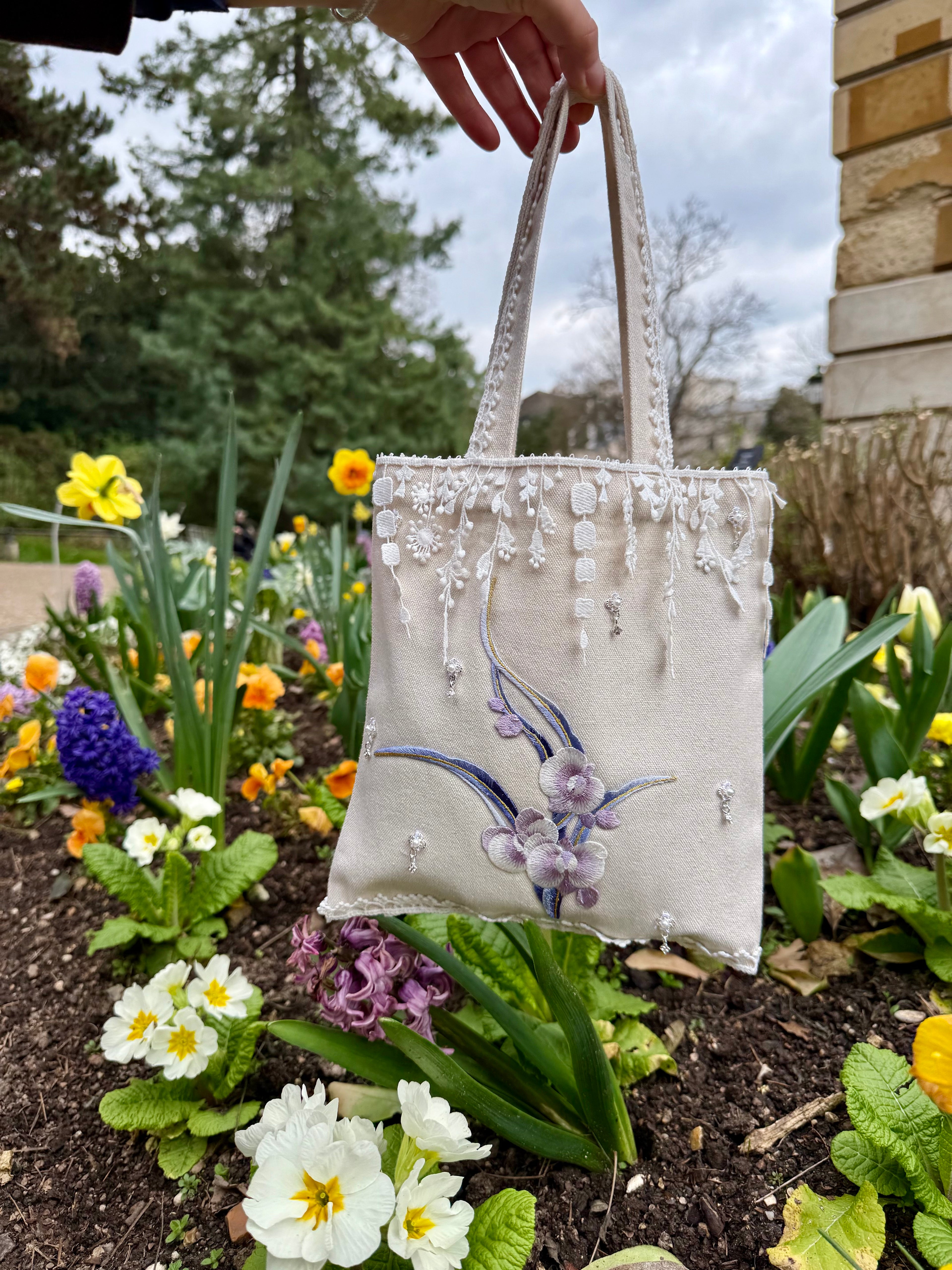 Handbag with floral design held over a garden with flowers