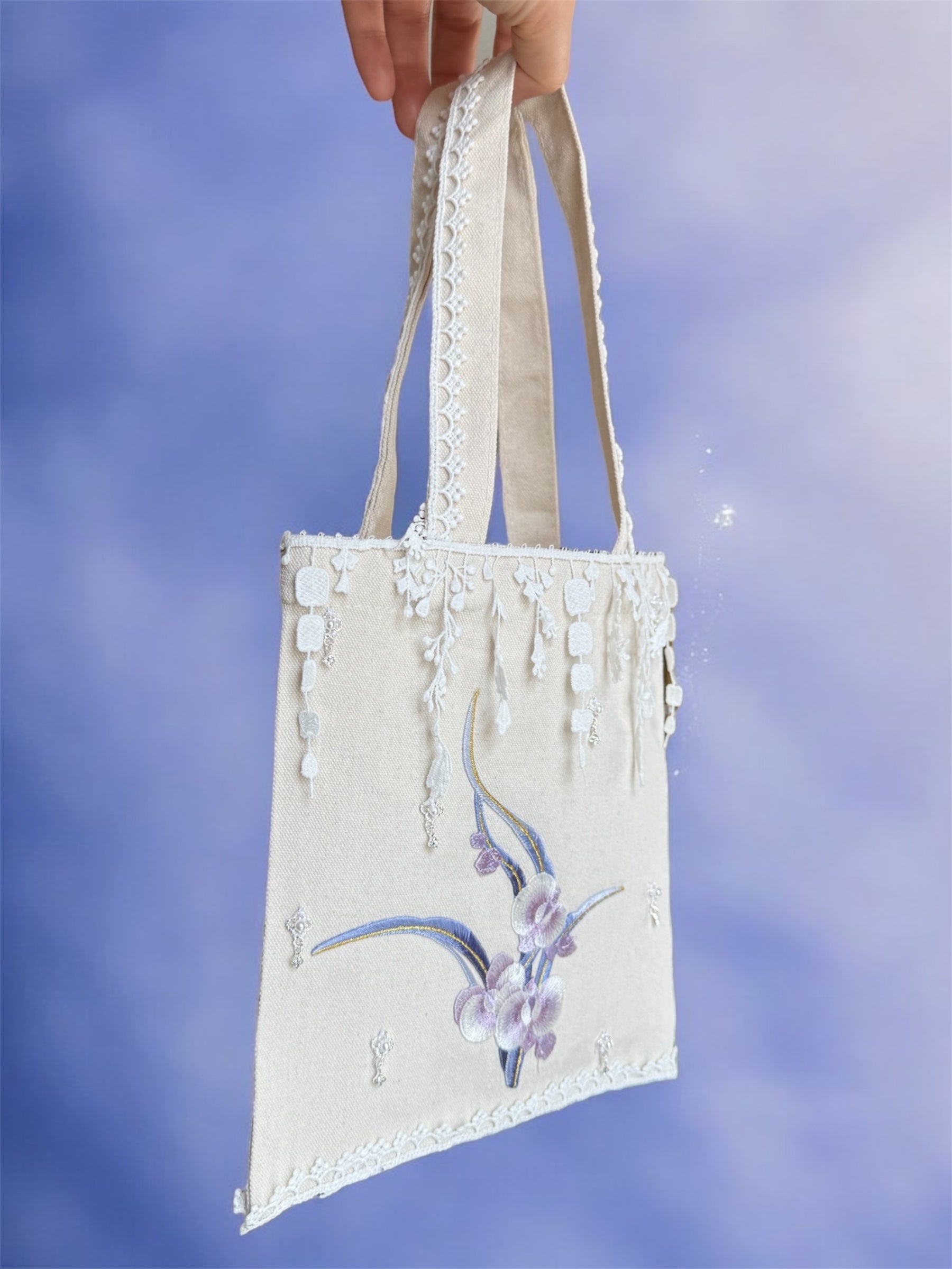 Hand holding a decorative tote bag with floral design against a blue sky background