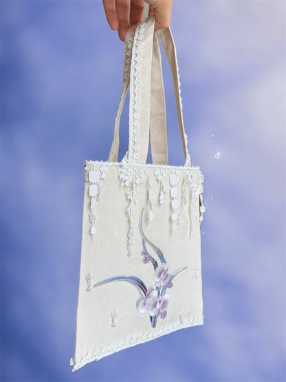 Hand holding a decorative tote bag with floral design against a blue sky background
